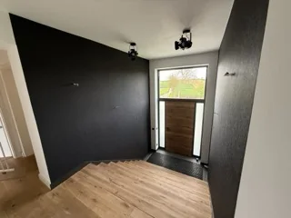 Innenraum mit dunkel gestrichenen Akzentwänden, hellem Boden und großen Fenstern