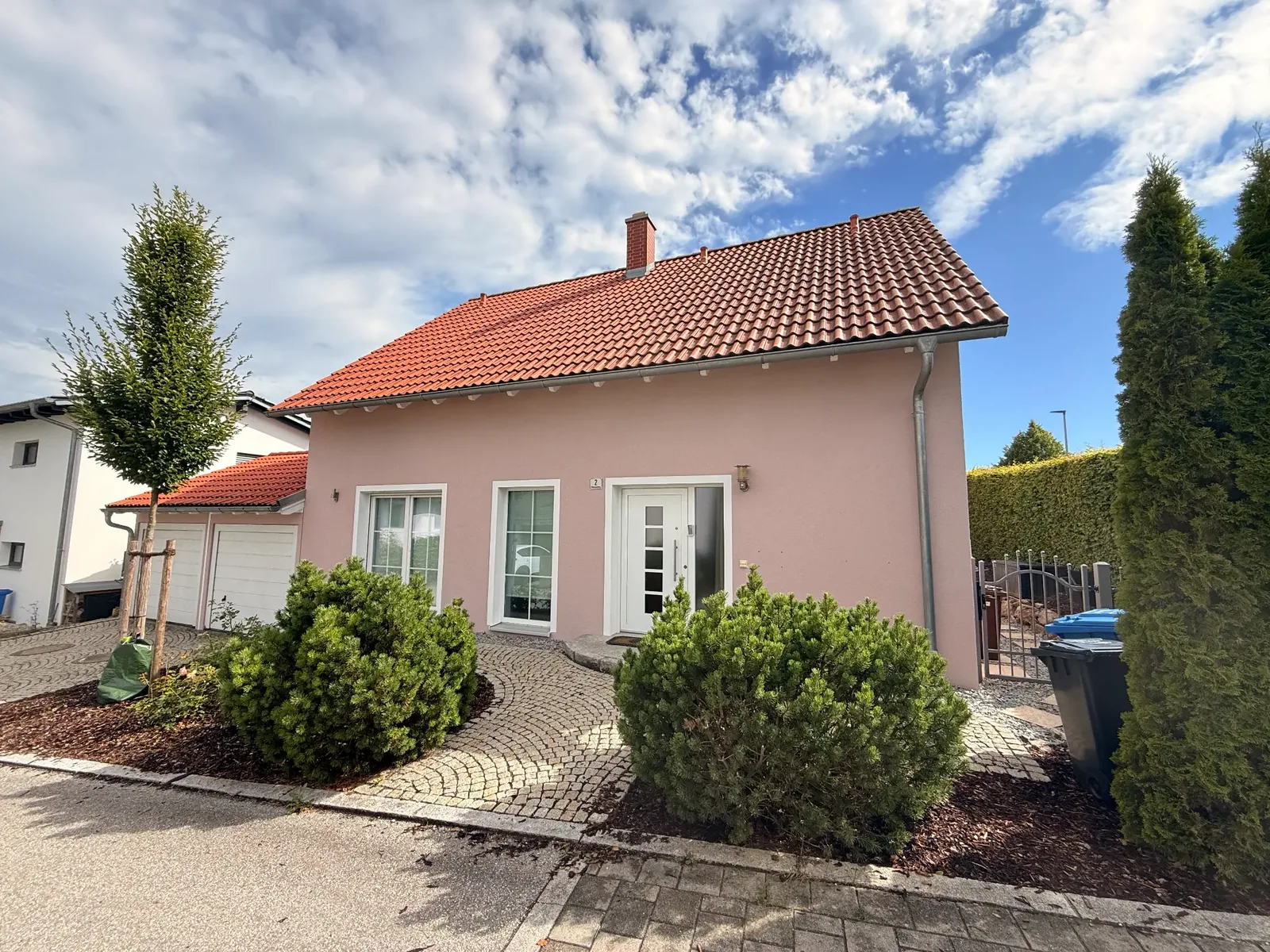 Einfamilienhaus mit rosafarbener Fassade, weißen Fensterlaibungen und rotem Ziegeldach